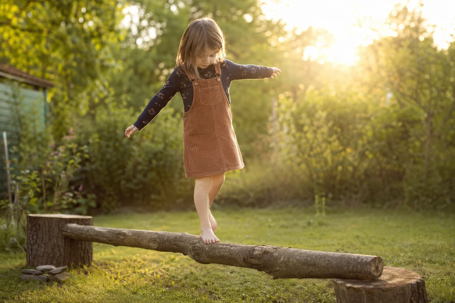 A child carefully balancing on a low log laid across two stumps in a backyard