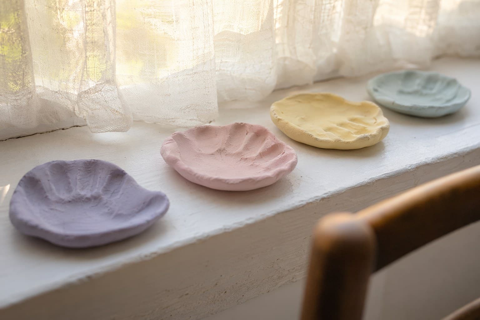 Child's hands pressing a handprint into a round air-dry clay dish on a sunlit kitchen table